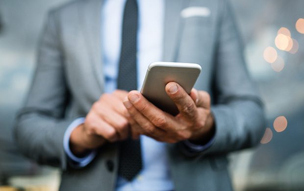 Unrecognizable businessman with smartphone standing in an outdoor hotel cafe. Man text messaging.